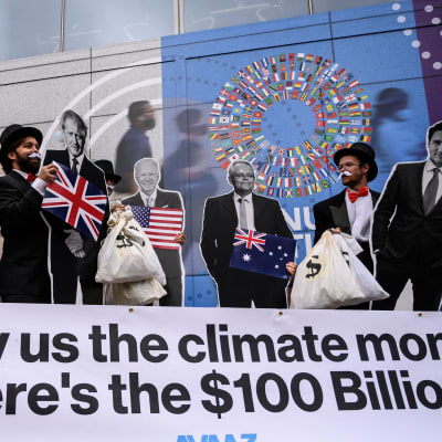 I mittenskiktet personer och kartongfigurer av människor. I förgrunden en text som frågar var 100 miljarder dollar av utlovade klimatpengar håller hus.