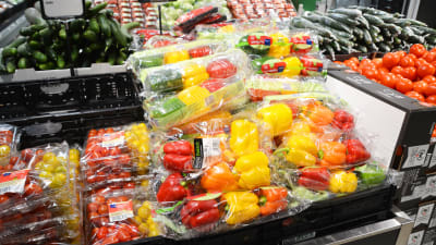 En hylla med gula, röda och gröna paprikor och tomater i plastpåsar.