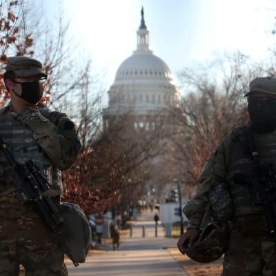 Två kamouflageklädda militärer med munskydd spanar med kongressens vita kupol i bakgrunden.