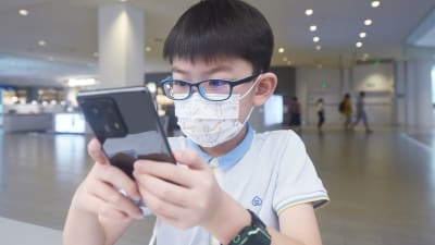 En pojke med glasögon använder en mobiltelefon.