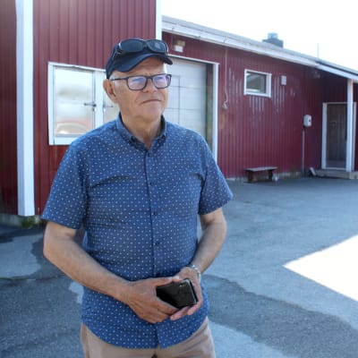 Man i blå skjorta står framför en röd byggnad.