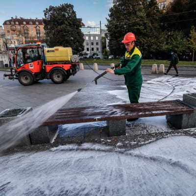 En man tvättar en bänk med högtrycksspruta i Moskva.