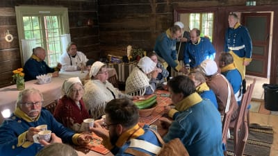 En grupp iklädd historiska kläder dricker kaffe i ett gammalt hus