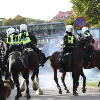 Poliser på polishästar rider på Göteborgs gator under en stor demonstration. Rök av en rökbomb syns på vilden. 