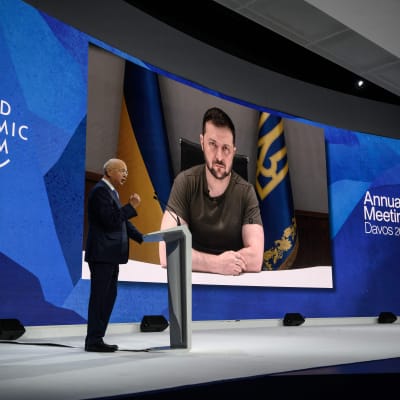 Klaus Schwab Davosin lavalla toivottaa etäyhteydellä osallistuvan Volodymyr Zelenskyin tervetulleeksi.