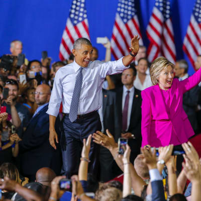 Demokraattien presidenttiehdokas Hillary Clinton pitää kampanjatilaisuuttaan yhdessä presidentti Barack Obaman kanssa. Charlotte, Pohjois-Carolina 5.7. 2016. Kuvassa parivaljakko vilkuttaa kansalle innokkaan ja vekkulin näköisinä.Taustalla liehuvat Yhdysvaltain liput.