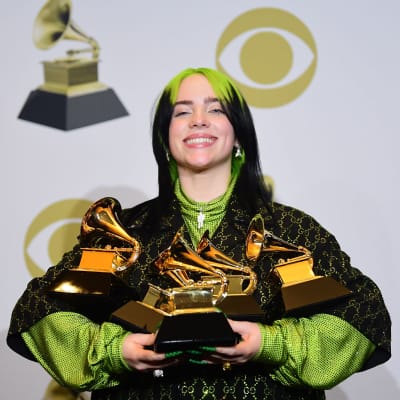Billie Eilish poserar med sina fem grammypriser som är formade som grammofoner i famnen. 
