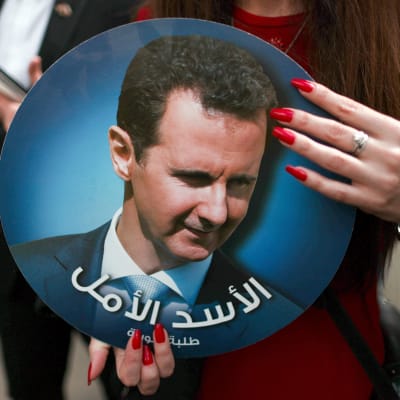 En kvinna som håller i ett porträtt av Syriens president Bashir al-Assad.  