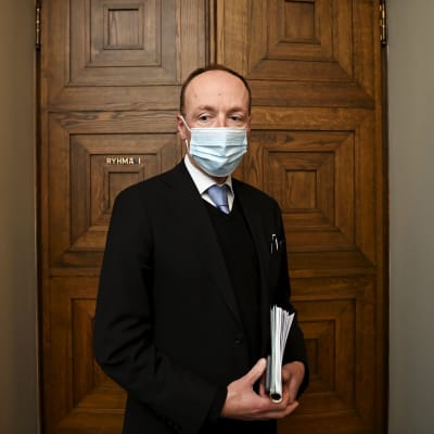 Jussi Halla-aho med munskydd framför riksdagsuppens mötsrum i riksdagen.