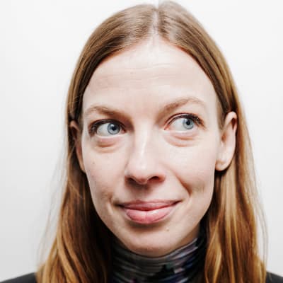 Li Andersson står vid en vit vägg och tittar åt sidan.