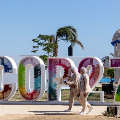 Två kvinnor går framför stora färgglada bokstäver på gatan, det står COP27
