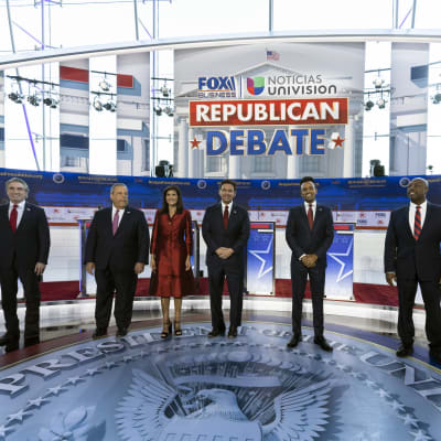 Sju republikanska kandidater står på scen inför en debatt. Sex är män och en är kvinna.