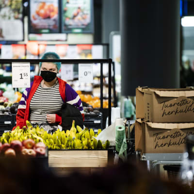 En kvinna står och tittar på prislappen på bananer i en större matbutiks frukt och grönt-avdelning.