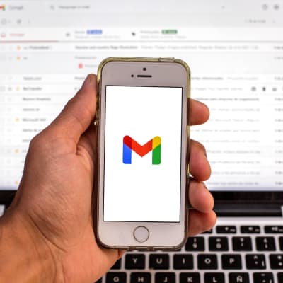 Henkilö pitää puhelinta kädessä ja puhelimen näytöllä näkyy Googlen gmail palvelun logo.