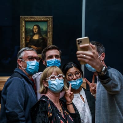 Joukko turisteja kasvomaskeissa poseeraa kuvattavana Mona Lisan edessä.