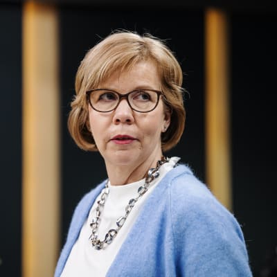 Kvinna med blå tröja och glasögon mot en svart bakgrund.
