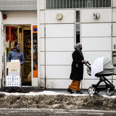 En kvinna i munskydd går med barnvagn i Helsingfors.