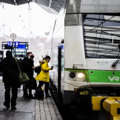 Tågresenärer stiger på ett grönt Intercitytåg på Helsingfors tågstation. 