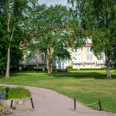 Ett gult hus står bakom flera träd.