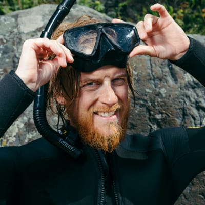 Juontaja Tom Nyludn maski ja snorkkeli päässä rannassa.