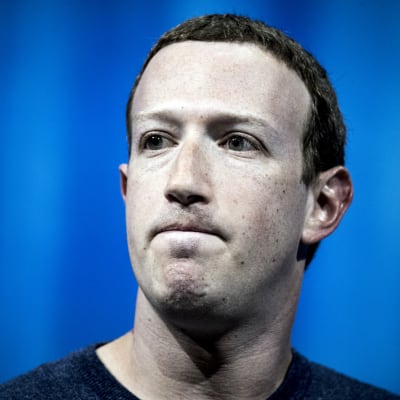 Facebooks grundare och vd Mark Zuckerberg med spänd min mot blå bakgrund. 