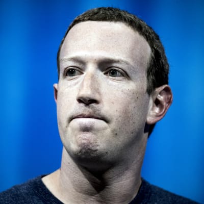 Facebooks grundare och vd Mark Zuckerberg med spänd min mot blå bakgrund. 