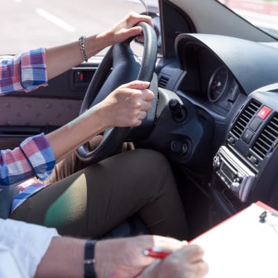 Bild på person som kör bil medan en annan gör anteckningar bredvid. 