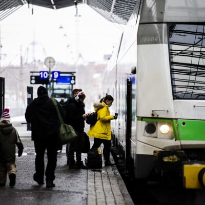 Tågresenärer stiger på ett grönt Intercitytåg på Helsingfors tågstation. 