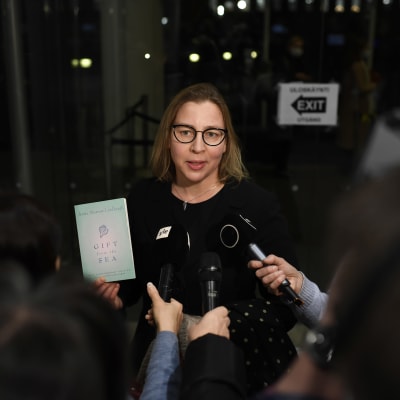 Tytti Yli-Viikari talar med journalister och håller i en bok.