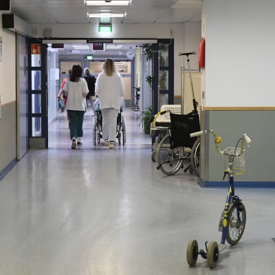 Sairaalan käytävä, potilas ja sairaanhoitajia.