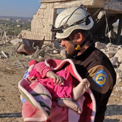 En medlem av frivilligkåren Vita hjälmarna bär på ett barn som räddats ur rasmassor i Maaret Misrin, Idlib, efter torsdagens flygattack utförd av syriska regeringsstyrkor.