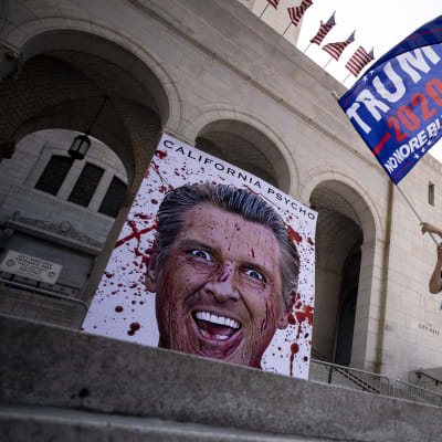 En demonstrant viftade med en kampanjflagga för återval av Trump utanför stadshuset i Los Angeles. Nidbilder på Kaliforniens guvernör Gavin Newsom förekom vid alla demonstrationer i Kalifornien på fredagen. 