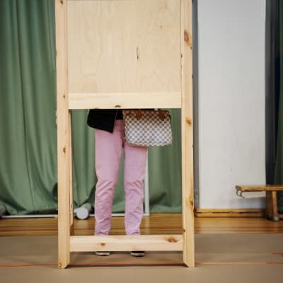 En person står i ett röstningsbås i en gympasal.