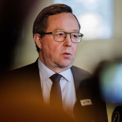 Näringsminister Mika Lintilä, en man i övre medelåldern med grånande hår och glasögon som bär kostym blir intervjuad framför en tv-kamera.