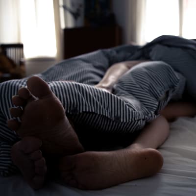 Fötterna på två sovande personer sticker delvis ut under ett täcke med randigt påslakan.
