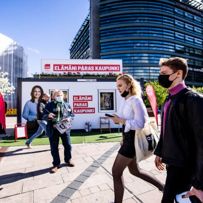 Socialdemokraternas valstuga i centrum av Helsingfors. Framför valstugan går en kvinna och en man med munskydd.