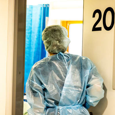 En vårdare iklädd skyddsutrustning går in i ett patientrum.
