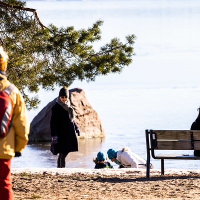 Ihmisiä nauttimassa rannalla aurinkoisesta säästä.