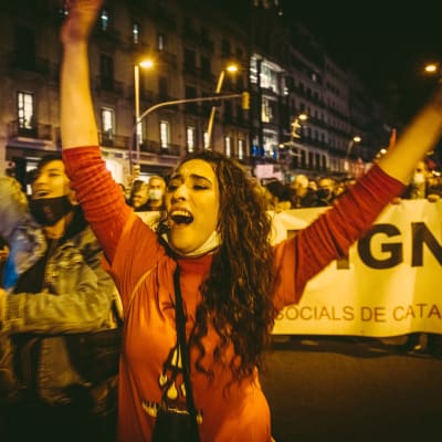 Nainen heiluttaa käsiään ja huutaa, taustalla ihmisiä ja mielenosoituslakana.