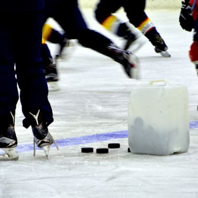 Jääkiekkokentällä on meneillään harjoitukset. Neljä jääkiekkoilijaa luistelee. 
