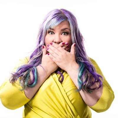 Jenny Lehtinen katsoo kameraan ja pitää käsiä suun edessä.