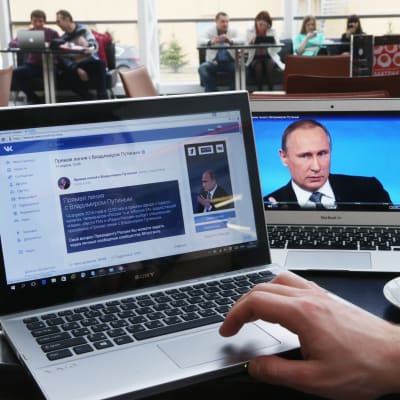 En kaffekopp och två bärbara datorer och på ett bord, på den ena skärmen syns Rysslands president Vladimir Putin och på den andra det populära ryska sociala nätverket en VKontakte.