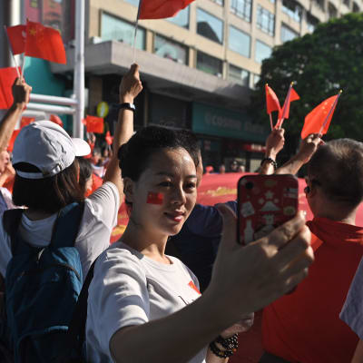 En kvinna med Kinas flagga målad på kinden tar en selfie under Kinas 70 års jubileum.