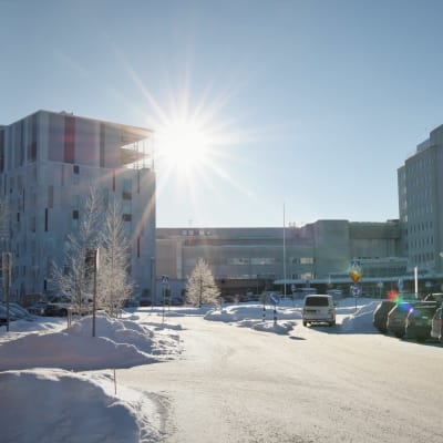 Ljusa byggnader i flera våningar, i förgrunden bilparkering och snö på marken.