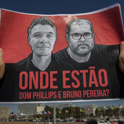 Två händer håller upp ett plakat som visar en bild av journalisten Dom Phillips och hans guide Bruno Pereira.