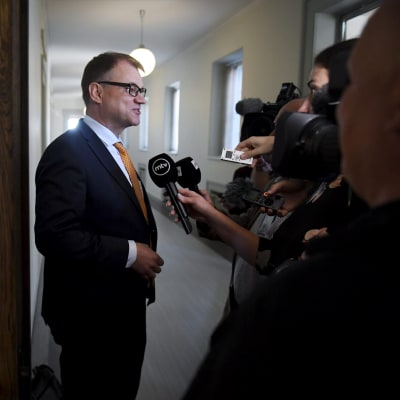 Juha Sipilä i riksdagens korridorer med journalister. 