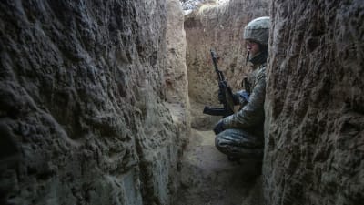 En soldat står på huk i en löpgrav