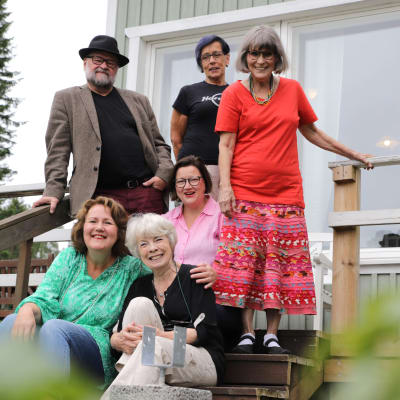 Viisi naista ja yksi mies istuu tai seisoo talon portailla ja hymyilee kameralle elokuun pilvipoutaisessa säässä.