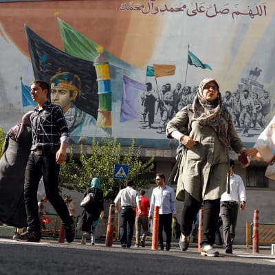 Iranier passerar en väggmålning med iranska martyrer och andliga ledare. Bilden tagen den 22 juli 2018 i Teheran. 