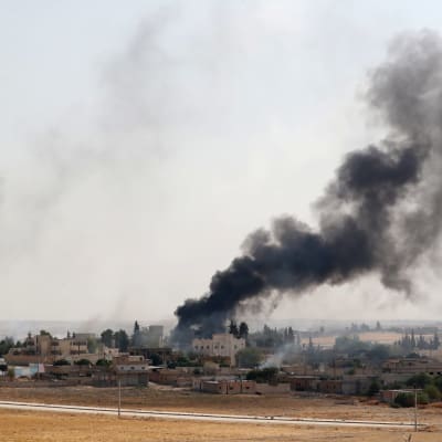En brinnande by i kurdkontrollerade områden. Byn ses på långt håll och det reser sig svart rök från byns centrum.